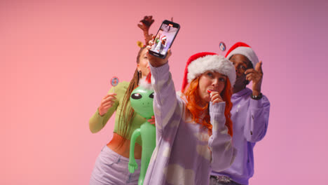 Studioaufnahme-Von-Freunden-Der-Generation-Z,-Die-Auf-Der-Weihnachtsfeier-Tanzen-Und-Für-Ein-Selfie-Posieren,-Mit-Weihnachtsmütze-Und-Rentiergeweih-1